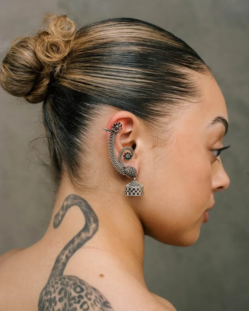 Side profile of a person with intricate ear piercings and tattoos on a neutral background
