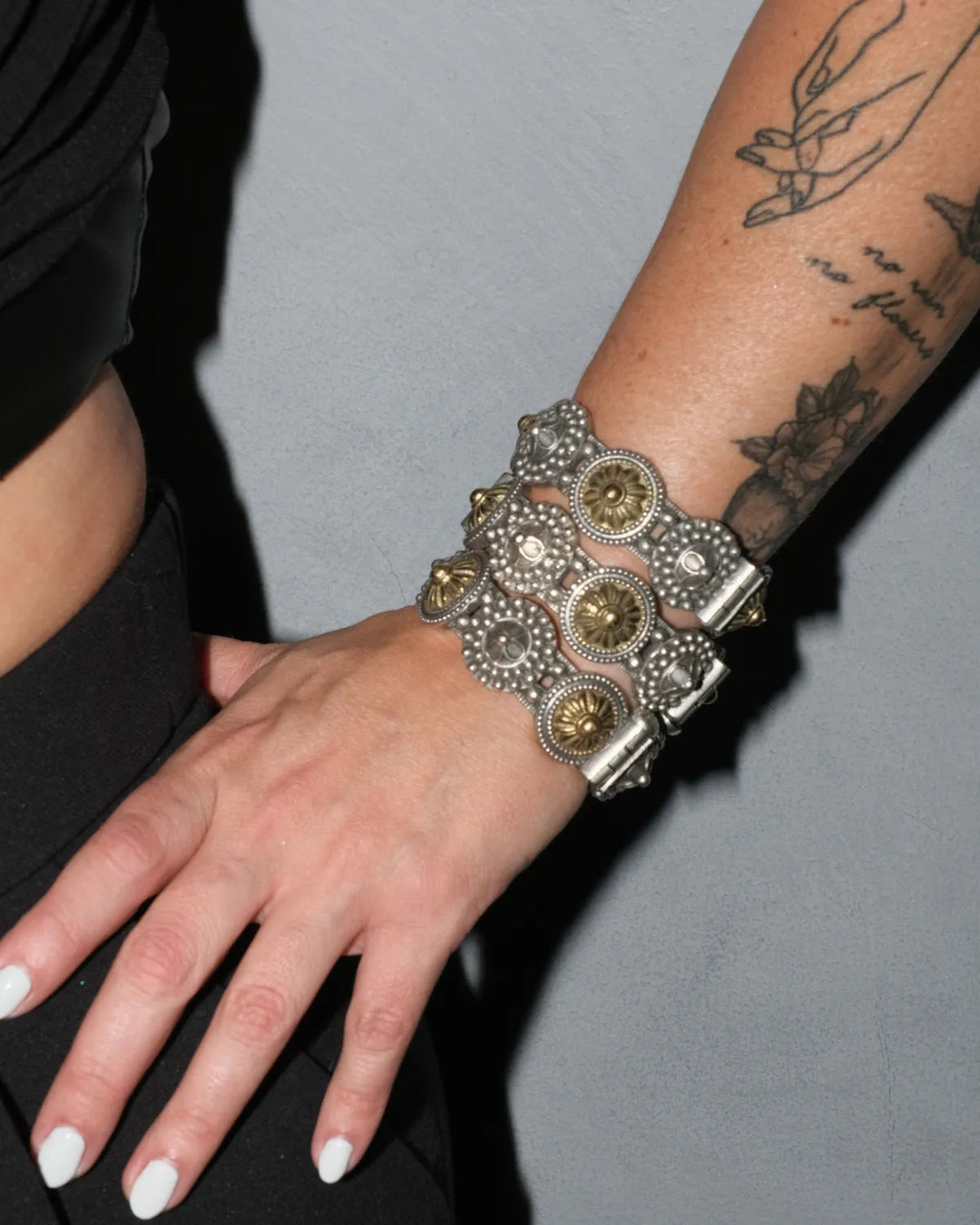 Decorative mixed metal gold and silver chunky bangles on a wrist with tattoos against a gray background