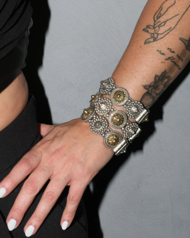 Decorative mixed metal gold and silver chunky bangles on a wrist with tattoos against a gray background