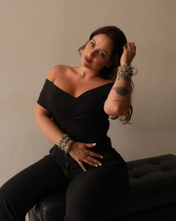 Woman in a black off-shoulder top sitting on a chair showing her chunky mixed metal bangles