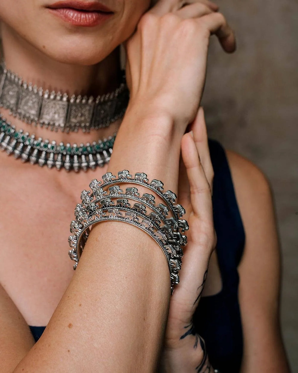 Close-up of a person wearing multiple pieces of silver jewelry including oxidised silver round bangles with decorative elephants