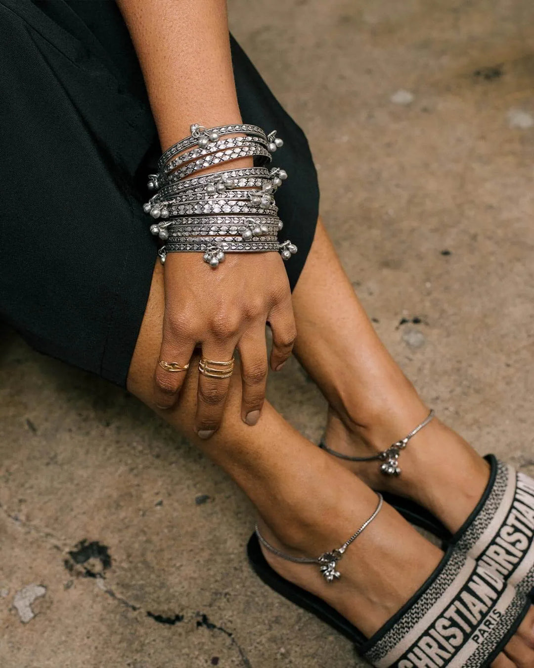 Close-up of hands with multiple silver bracelets on a concrete surface
